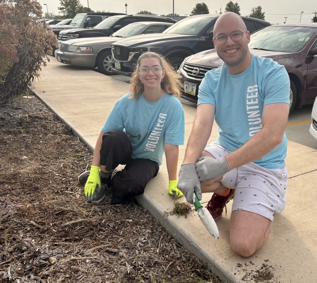 Two volunteers gardening near cars.