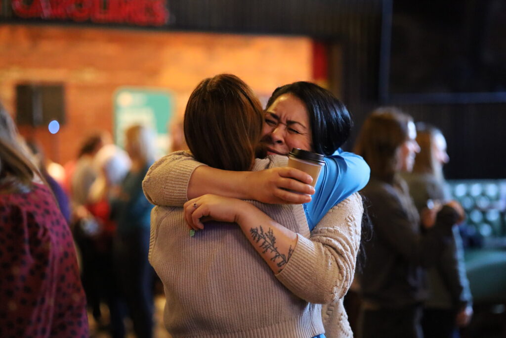Two women embracing joyfully indoors.